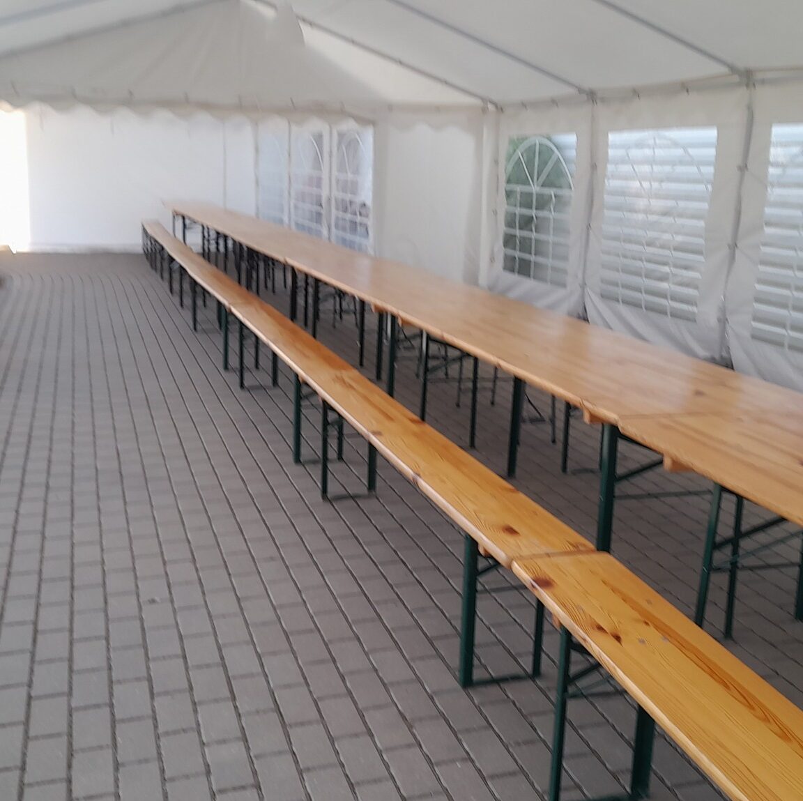 Front Page ant trinkelių pastatyti mediniai stalai ir suolai, viskas yra baltoje palapinėje