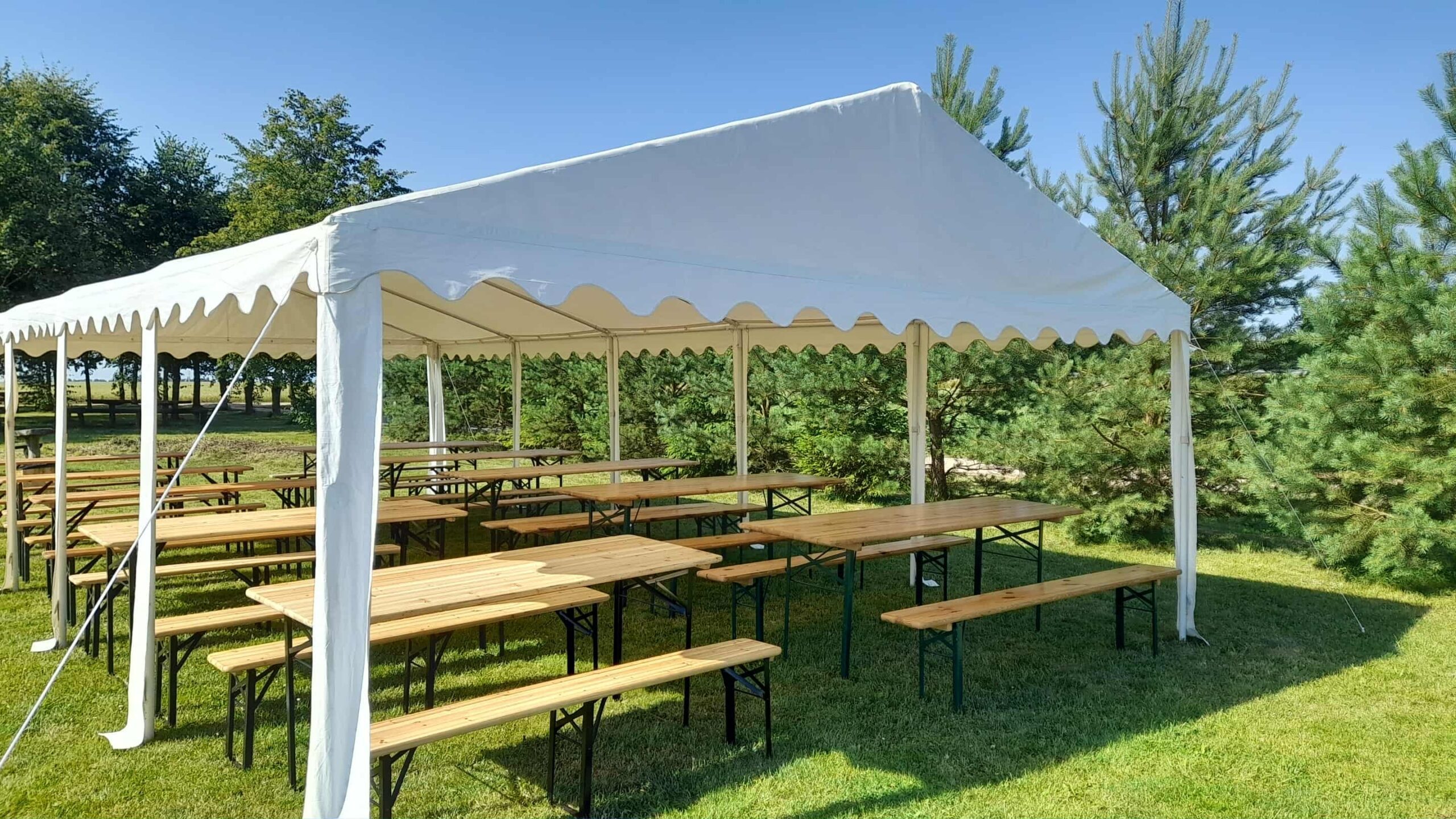 atvira palapinė baltu stogu ir mediniai stalai, suolai, sustatyti palapinėje eilėmis