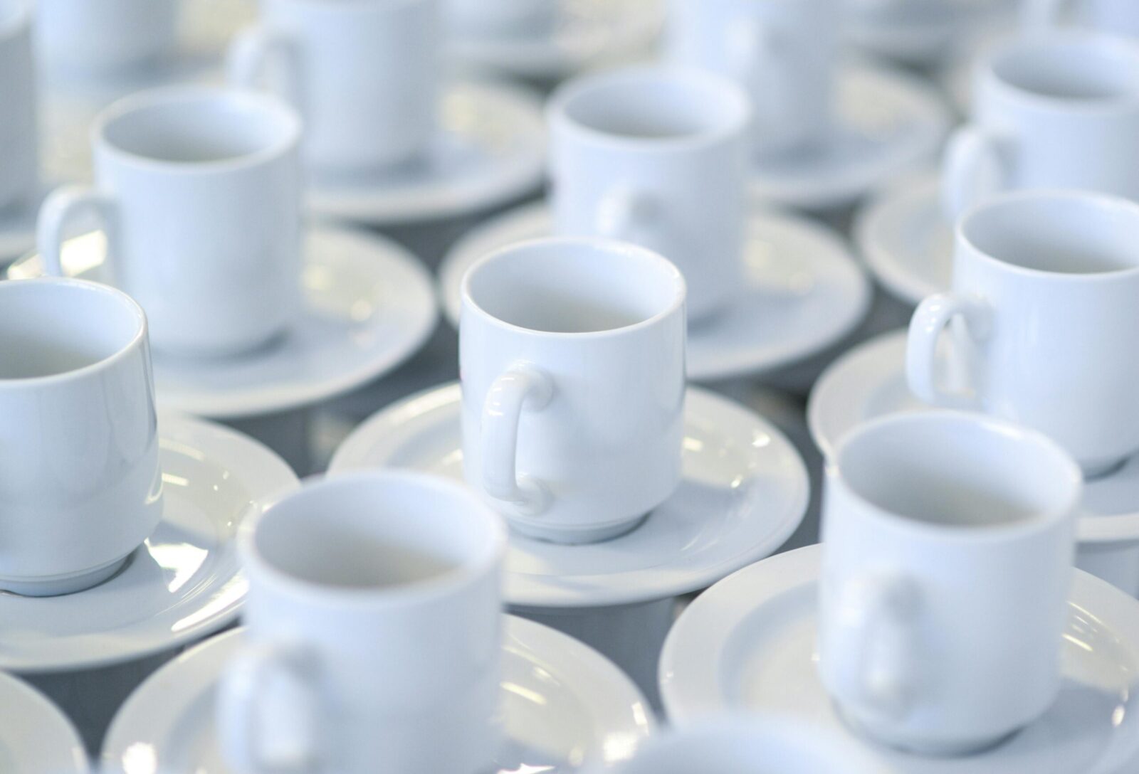 Multiple white ceramic coffee cups arranged neatly on saucers, ideal for dining or catering settings.